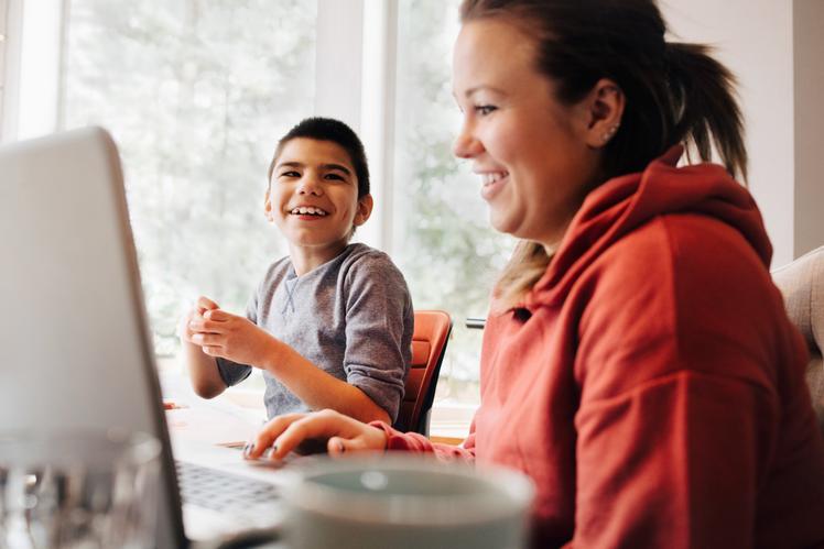 Lachende vrouw en kind met laptop aan de eettafel