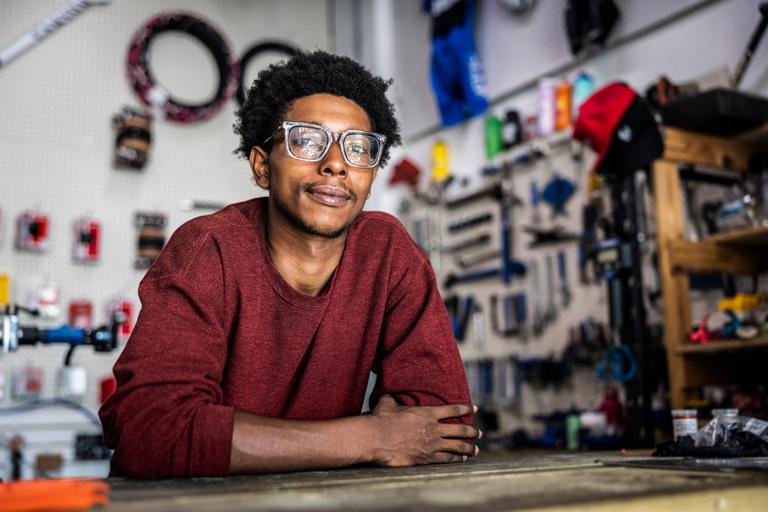 Man met bril leunt op werkbank in werkplaats