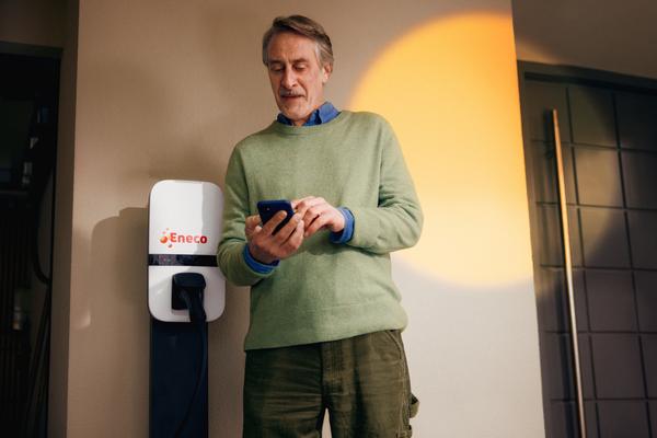 een man voor een laadpaal kijkt naar zijn telefoon