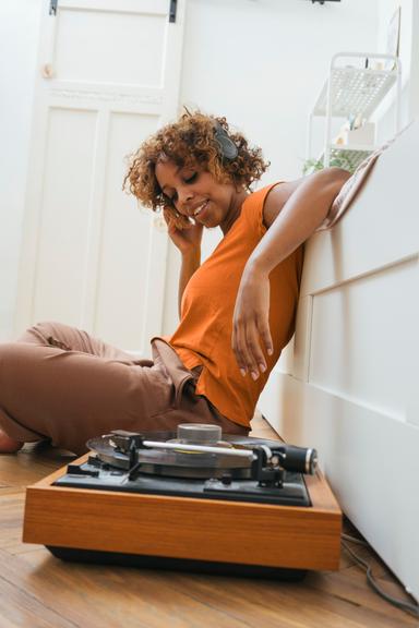 Vrouw met koptelefoon zit op de grond naast platenspeler en luistert naar muziek