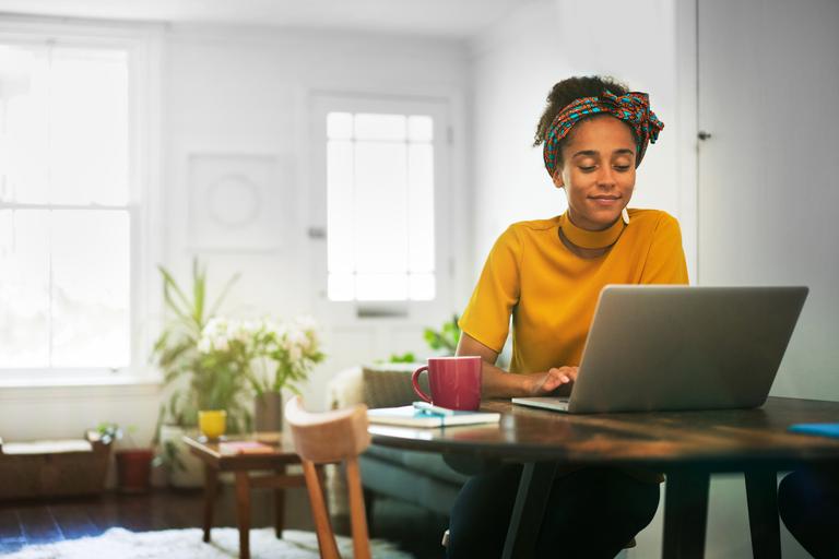 Vrouw zit in woonkamer aan de keukentafel met een laptop