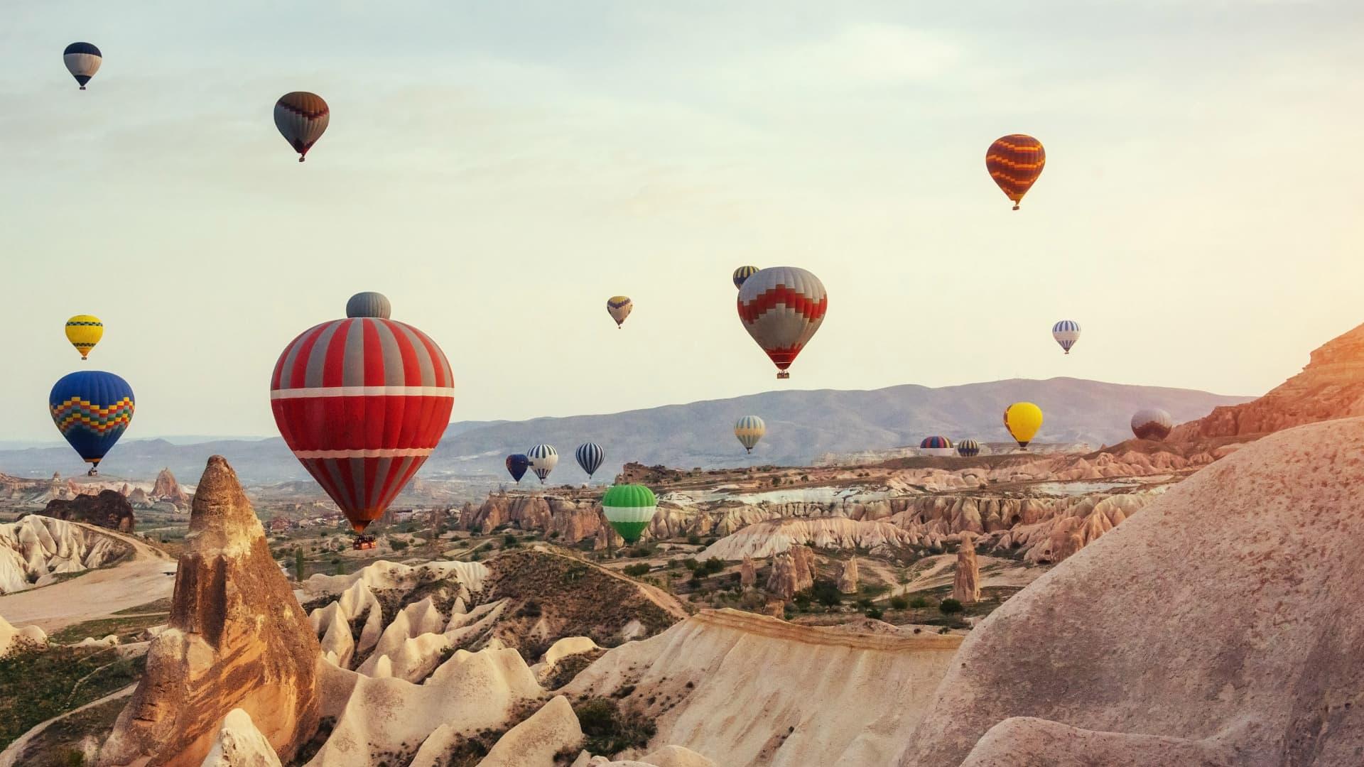 Colorful hot air balloons flying over unique rock formations at sunrise in Turkey.