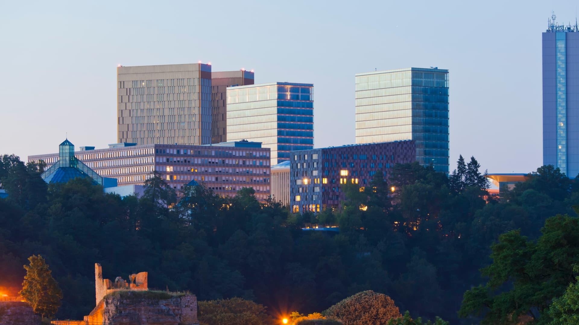 Luxembourg city skyline at twilight with illuminated buildings and greenery in the foreground.